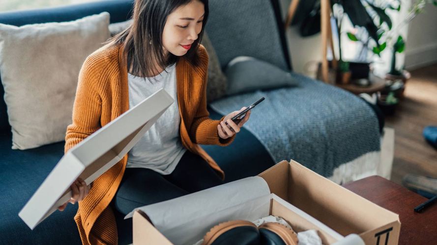 A woman looks at a phone while opening a shoebox: consumer goods data.