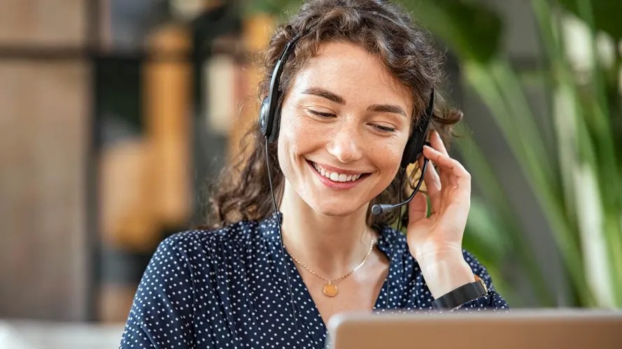 A woman wears a headset and works at a laptop, possibly impacting contact centre revenue.