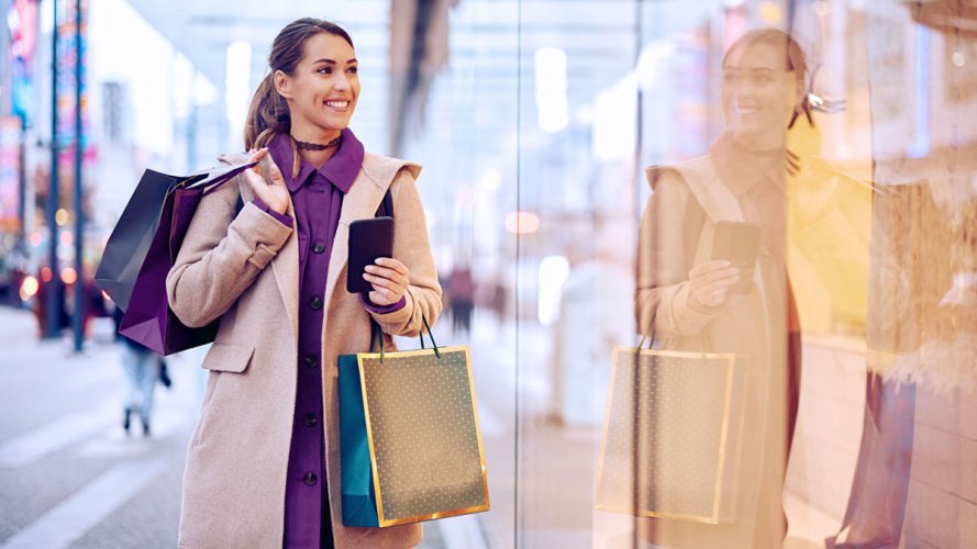 A photo of a shopper carrying shopping bags and a mobile phone, walking down the street: holiday shopping predictions.