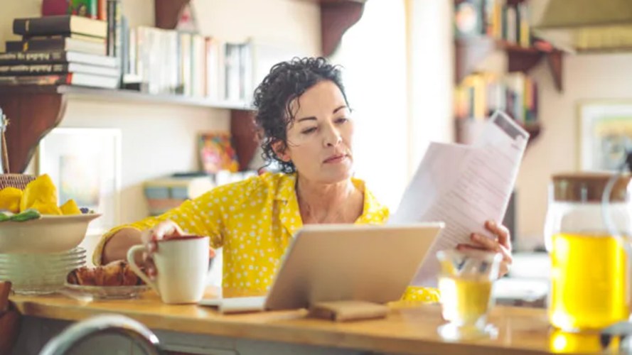 A woman sitting at a table with a coffee mug in one hand, and a newspaper in the other hand