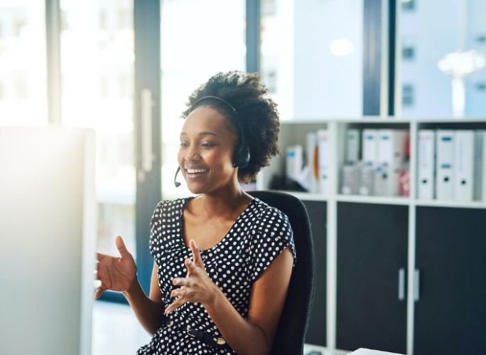 Smiling black woman with headset seated at a computer