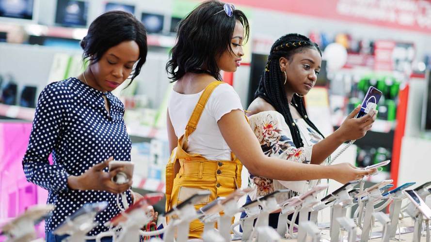 three people shopping for smartphones in a store, a common consumer behavior trend