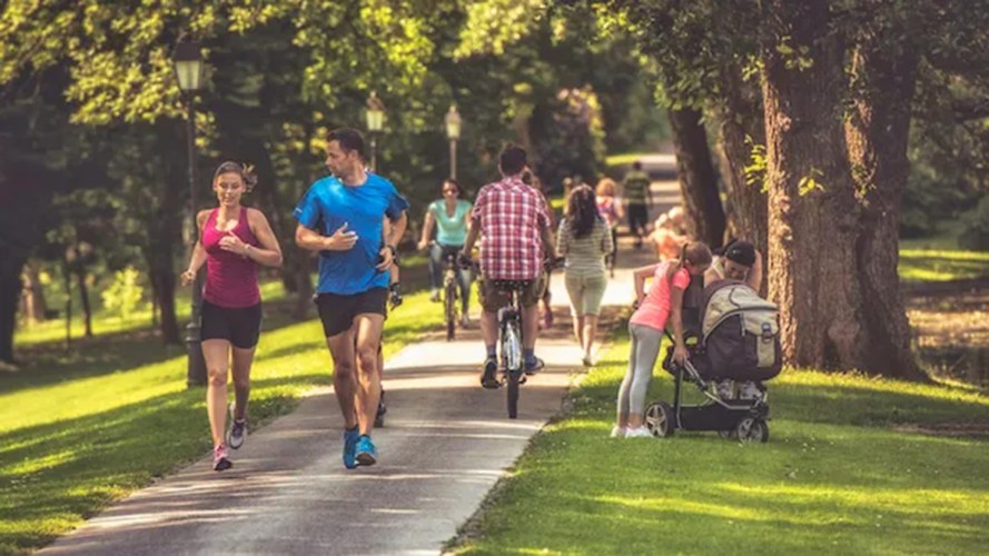 A group of people walking through a park, with the focus on a man and woman jogging