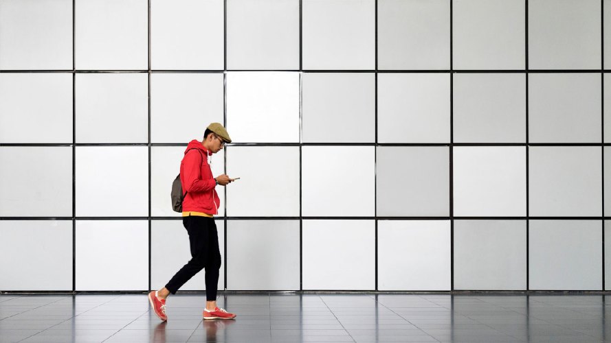 guy walking in front of a white wall looking at his phone CXO