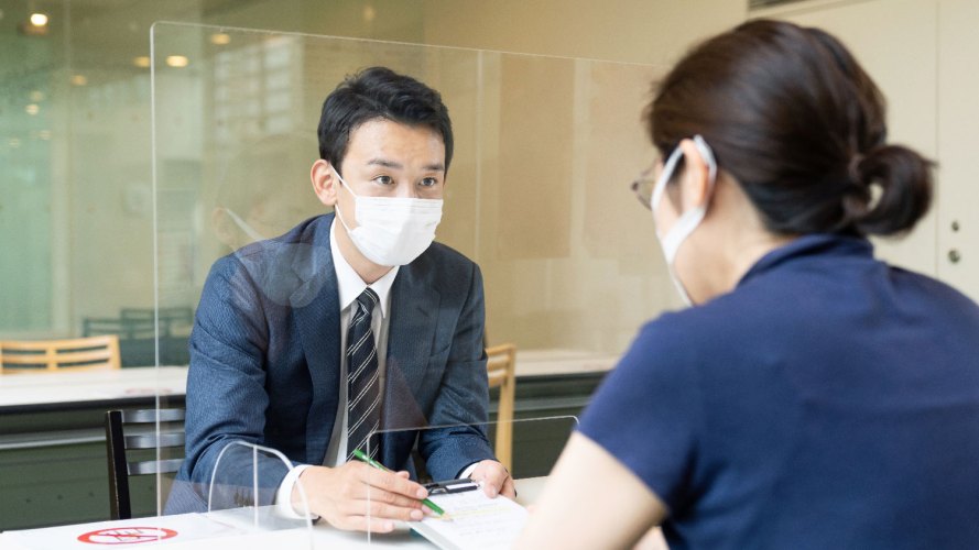 man and woman on opposite site of glass screen wearing masks public sector