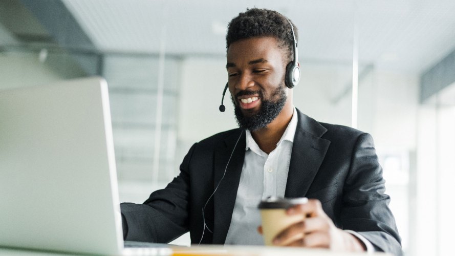 Customer service agent with headset on and coffee in one hand looking at his laptop screen — automate business processes: IT, CIO
