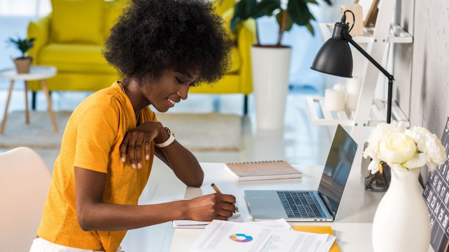 woman in a yellow blouse in front of her laptop looking at a graph on her desk and taking notes - unified data connected customer