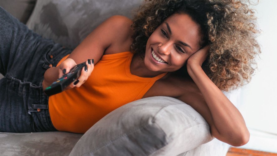 woman laying on couch with TV remote in her hand: subscription management