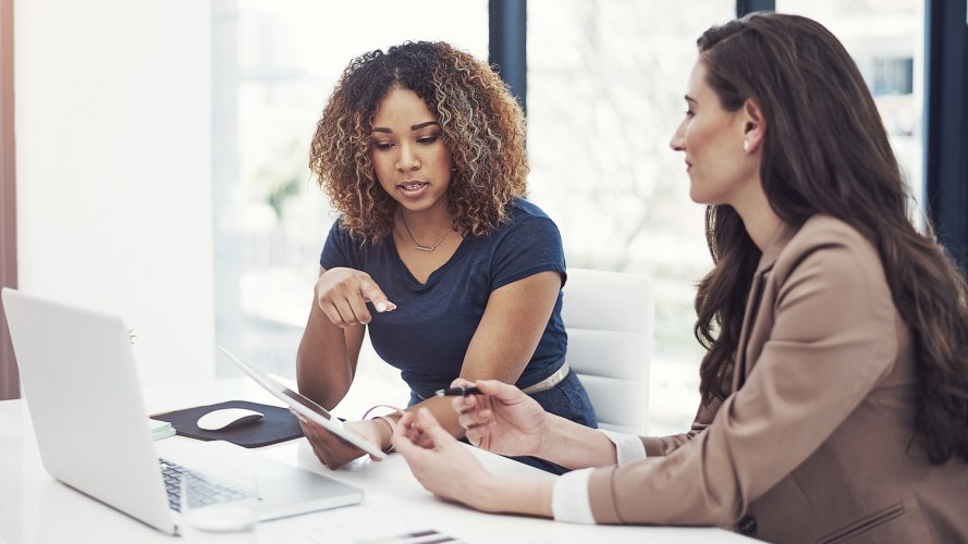 Two businesswomen in an office look at a tablet, exploring ways to use AI for wealth management