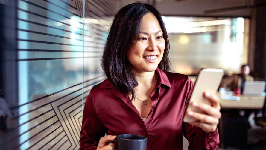 woman in office setting holding a coffee mug and looking at her phone. revenue leaders growth