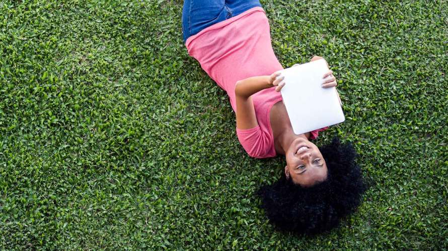 A photo of a woman lying on her back on the grass looking at a tablet: Reducing customer churn