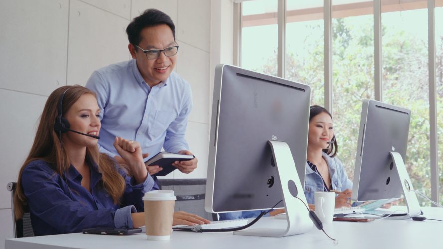 A group of customer service agents working at a desk with monitors. DEI training.