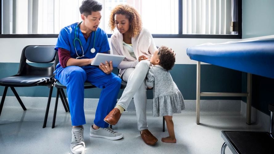 male healthcare professional sitting with a mother and child looking at files