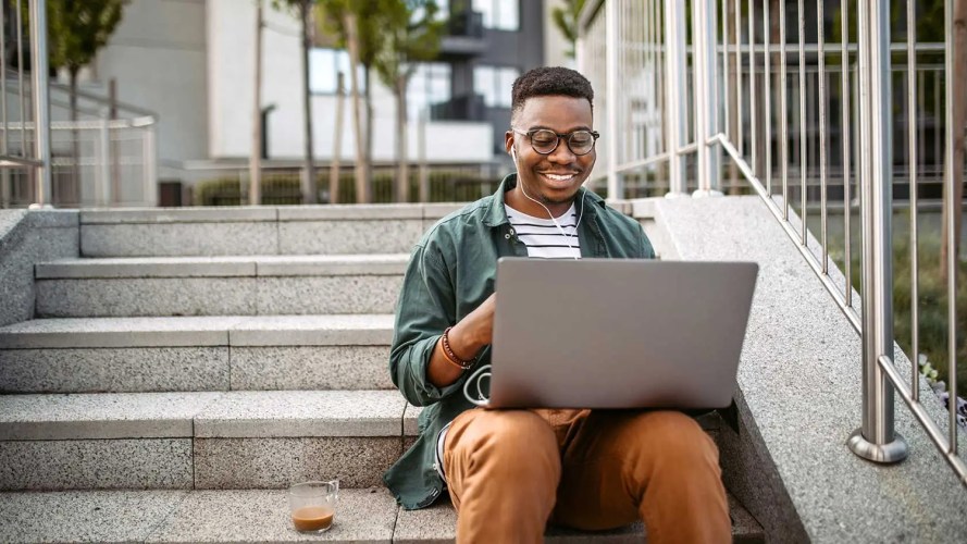 A student sitting on stairs and looking at their laptop