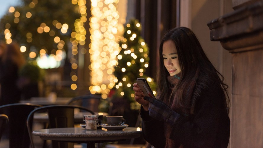 A woman sits outside a cafe using her phone for a retail shopping experience