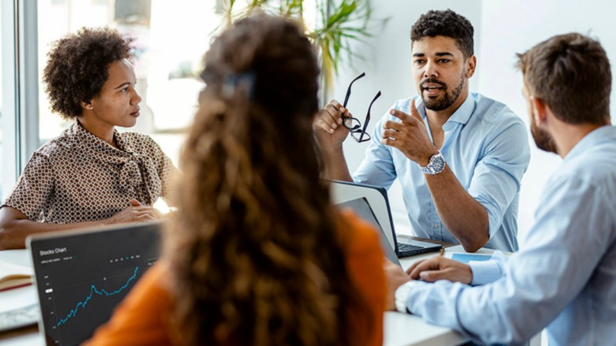 A group of four people sitting around a table and talking about a stock chart