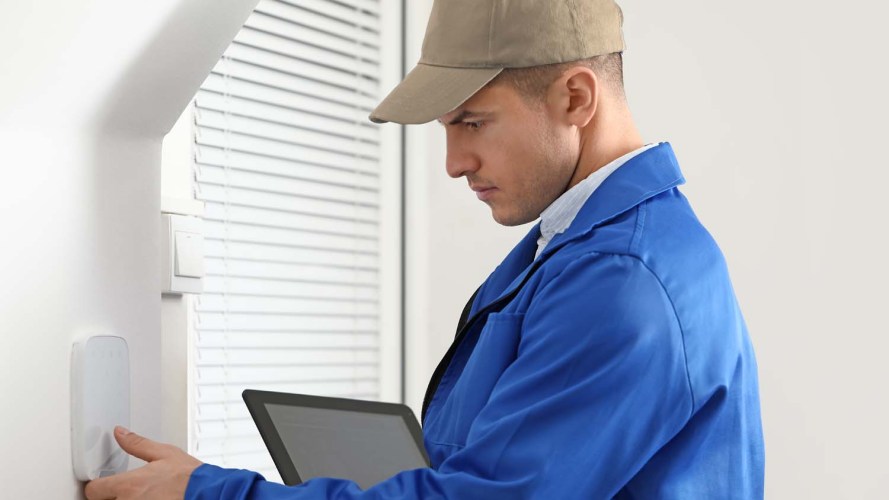 Service representative, dressed in a blue jacket and khaki hat, performing proactive field service on a panel inside of a home painted in white / reduce operating costs