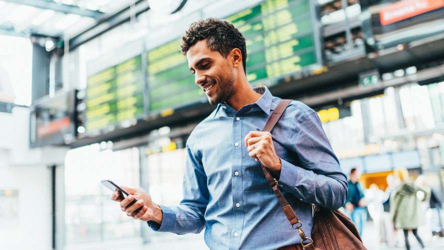 Passenger in an airport, checking flight updates on his phone while standing in front of departures board / what is real-time marketing