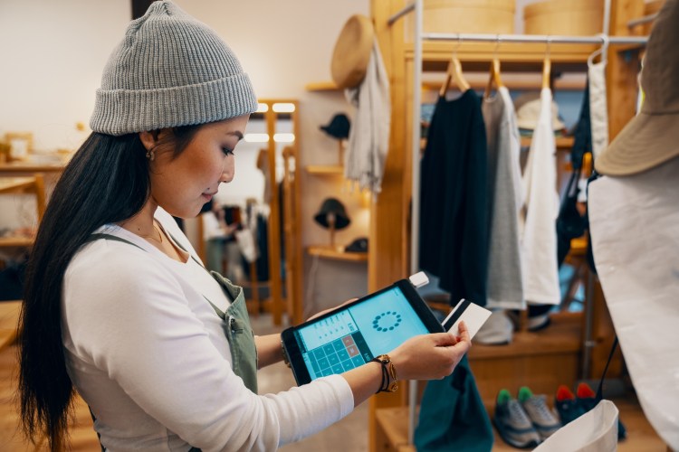 Retail shop clerk viewing consumer goods industry trends on a digital tablet in her store.