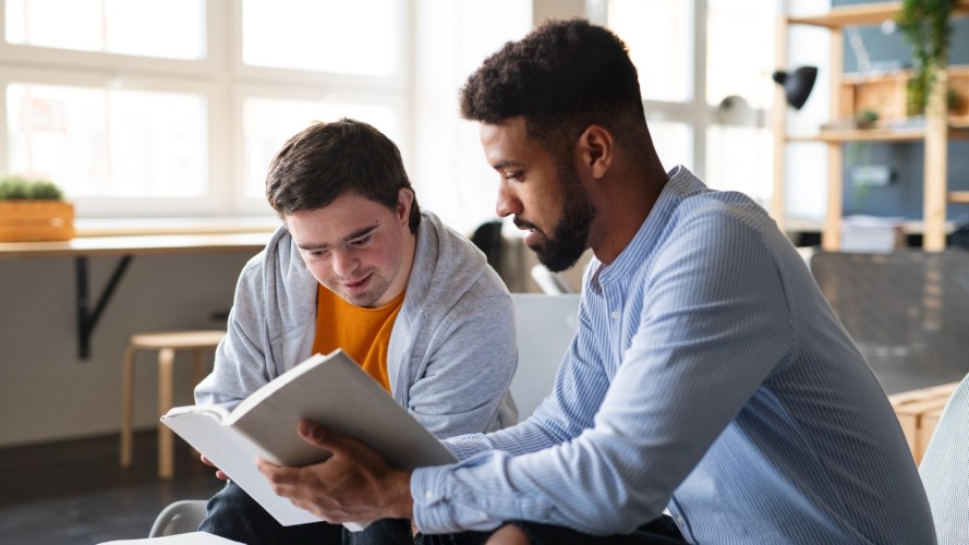 A young man read a book with another young man. These efforts will be helped by nonprofit CRM tools.