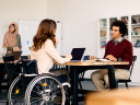 An employee in a wheelchair works with other employees in an office setting: DEAM