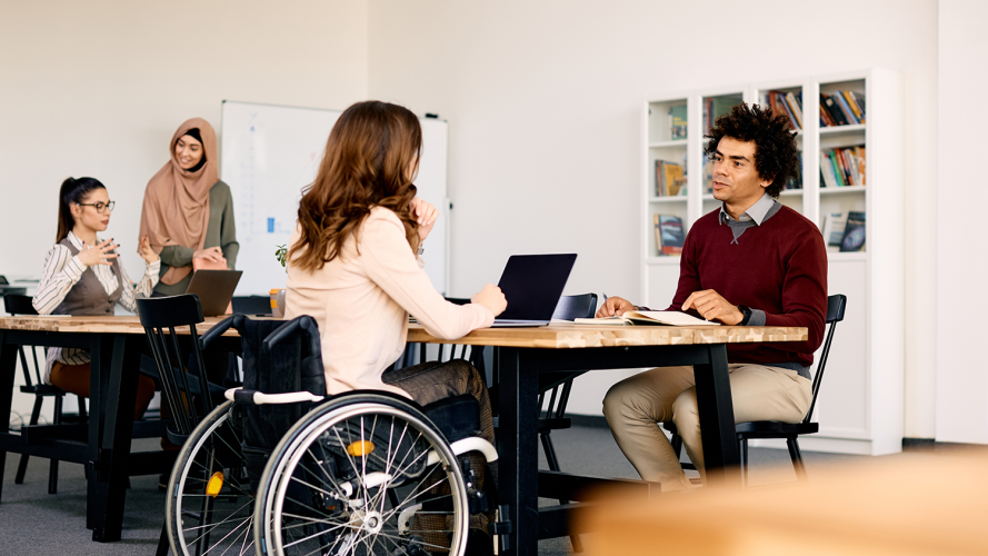 An employee in a wheelchair works with other employees in an office setting: DEAM