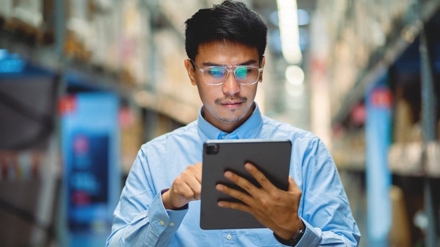 A man in glasses and a blue shirt uses a digital tablet for asset service management