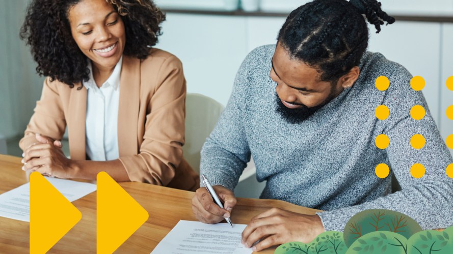 Two people smiling and sitting at a table while signing a sales contract.