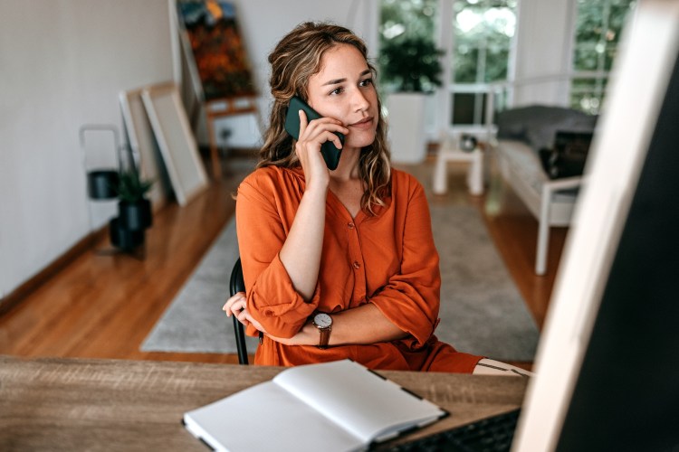 Young woman talking on smart phone at home office - stock photo.