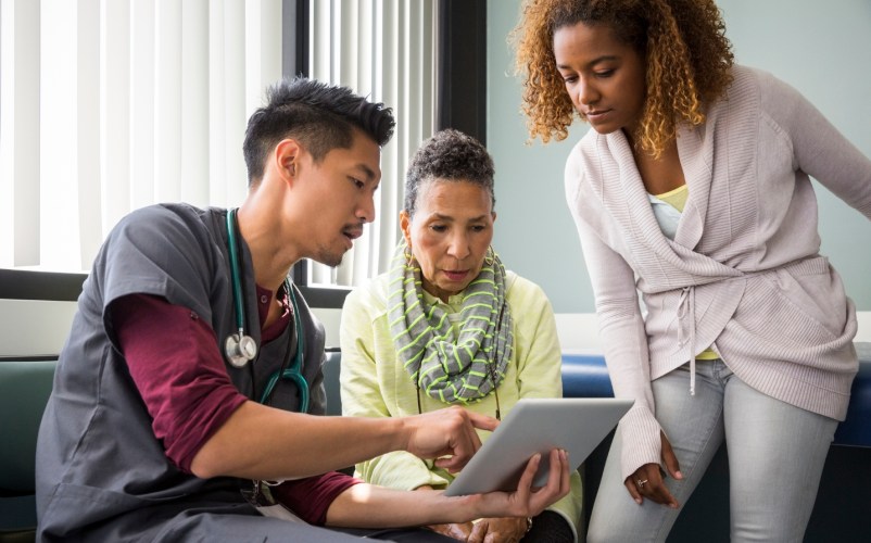 Male nurse working to improve the patient experience with two patients in an exam room.