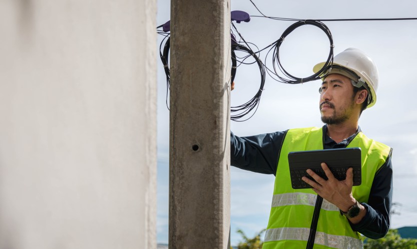 A telecom worker in a hard hat checking wires atop a utility poll.