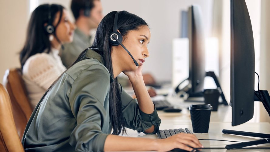 A call center agent sits at their desk, looking exhausted and overwhelmed.