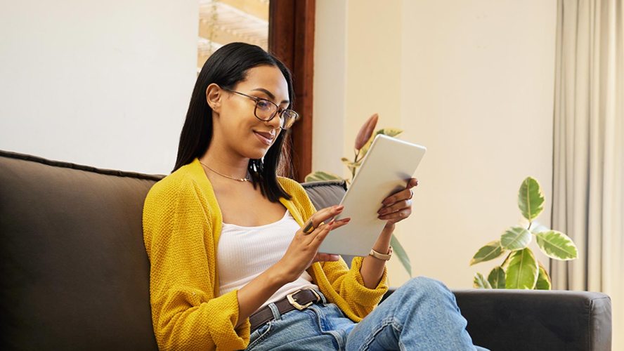 A woman wearing glasses and a yellow sweater completes a customer satisfaction survey on her digital tablet