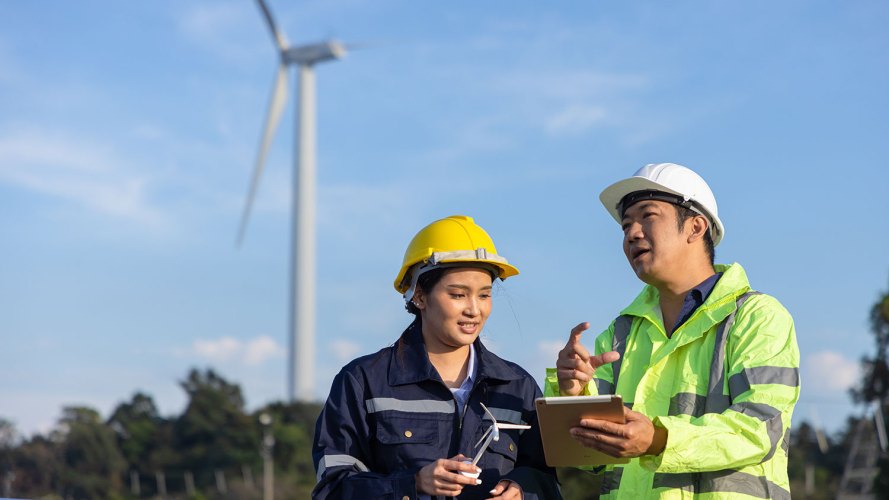 Two technicians in hard hats use technology to support field service sustainability.