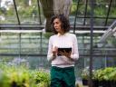 A woman in a greenhouse with a tablet conducting a nature positive policy for her business.