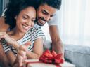 A man surprises a woman with a wrapped gift box, probably inspired by retail data from holiday shoppers.