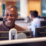 Homem sorrindo, sentado em frente ao computador, realizando uma chamada com o cliente.