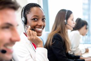 Mulher atendendo um cliente via chamada telefônica enquanto olha sorrindo para a câmera.