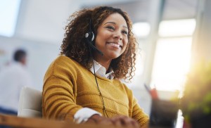 Profissional de atendimento ao cliente sorri enquanto utiliza fone de ouvido.