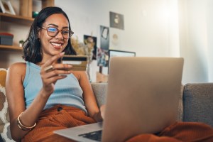 Mulher navega em notebook enquanto segura um cartão de crédito.