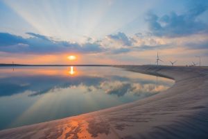 campo aberto, lago no meio e ao fundo engrenagens para gerar energia do vento