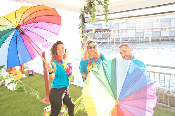 Three people smiling and holding rainbow umbrellas