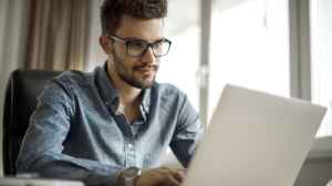 Ein junger Mann mit Brille arbeitet am Schreibtisch auf einem Laptop