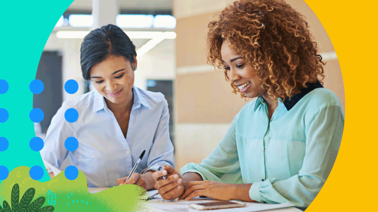 Zwei Frauen sitzen im Büro an einem Tisch und haben Stift und papier in der Hand