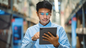 Ein Mann steht in einer Lagerhalle und hält ein Tablet in der Hand.