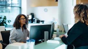 Woman behind a desk talks with another woman in an office setting / increase trust in government services