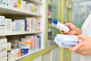 Close up de una mano tomando medicamentos de una góndola de farmacia.