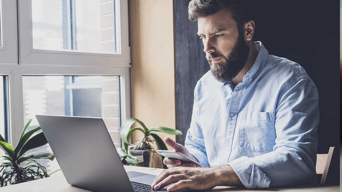 Man working by window in office using wireless digital gadgets for projects.