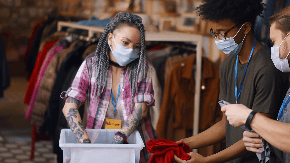 volunteers in safety mask packing clothes in boxes for charity